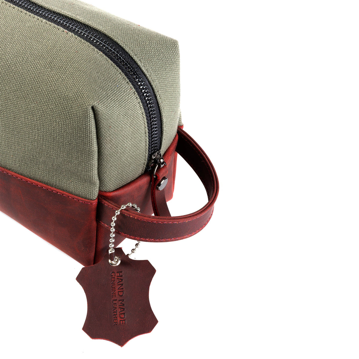 An olive green canvas travel pouch with a dark red leather handle and trim, featuring a hanging leather tag that reads 'HAND MADE IN ITALY'.