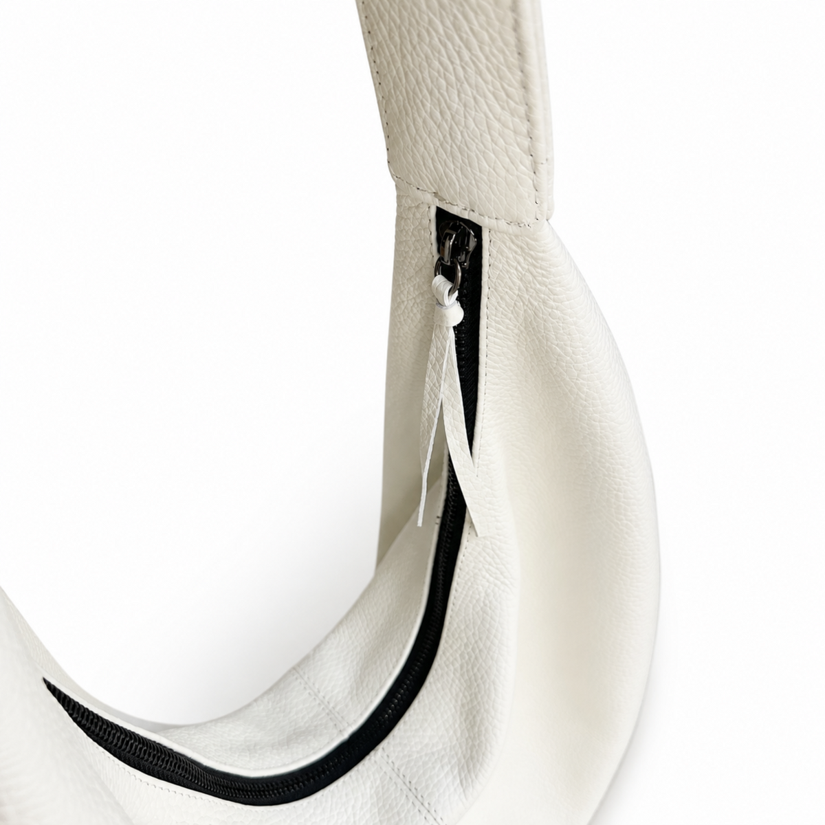 Close-up of a white pebbled leather shoulder bag showing a black zipper with a white pull tab on a white background.