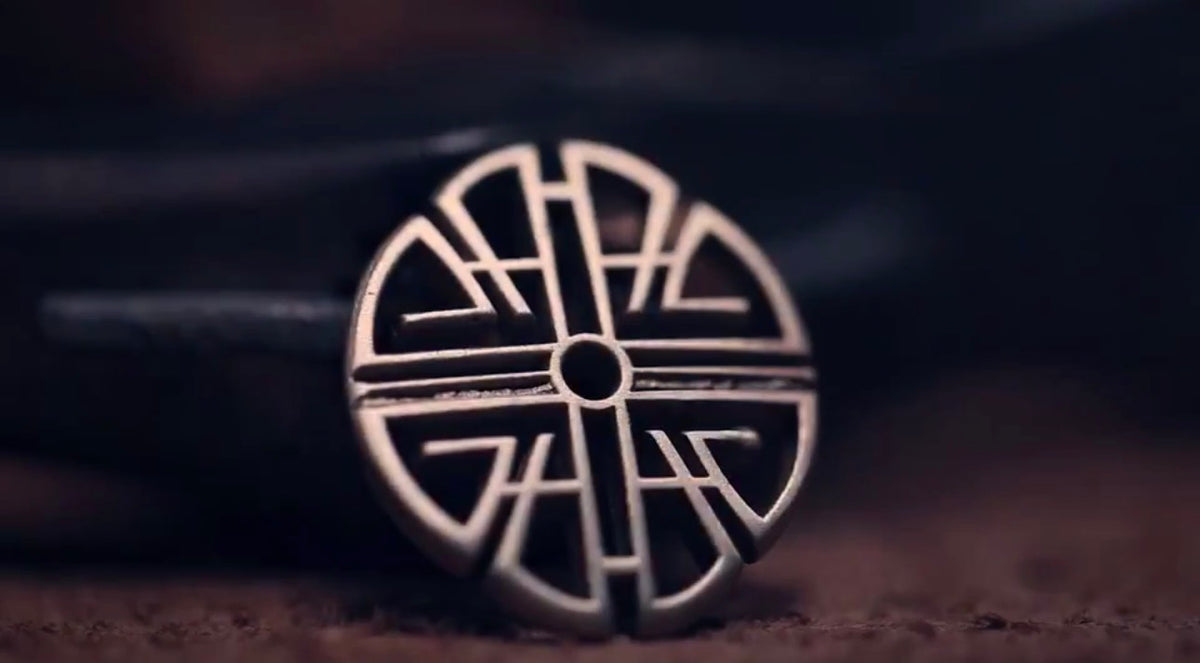 A circular silver-toned metal ring with an intricate geometric cutout pattern, resting on a dark textured surface.